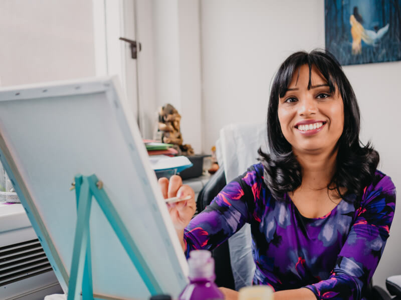 A woman sitting at a paint canvas smiling.